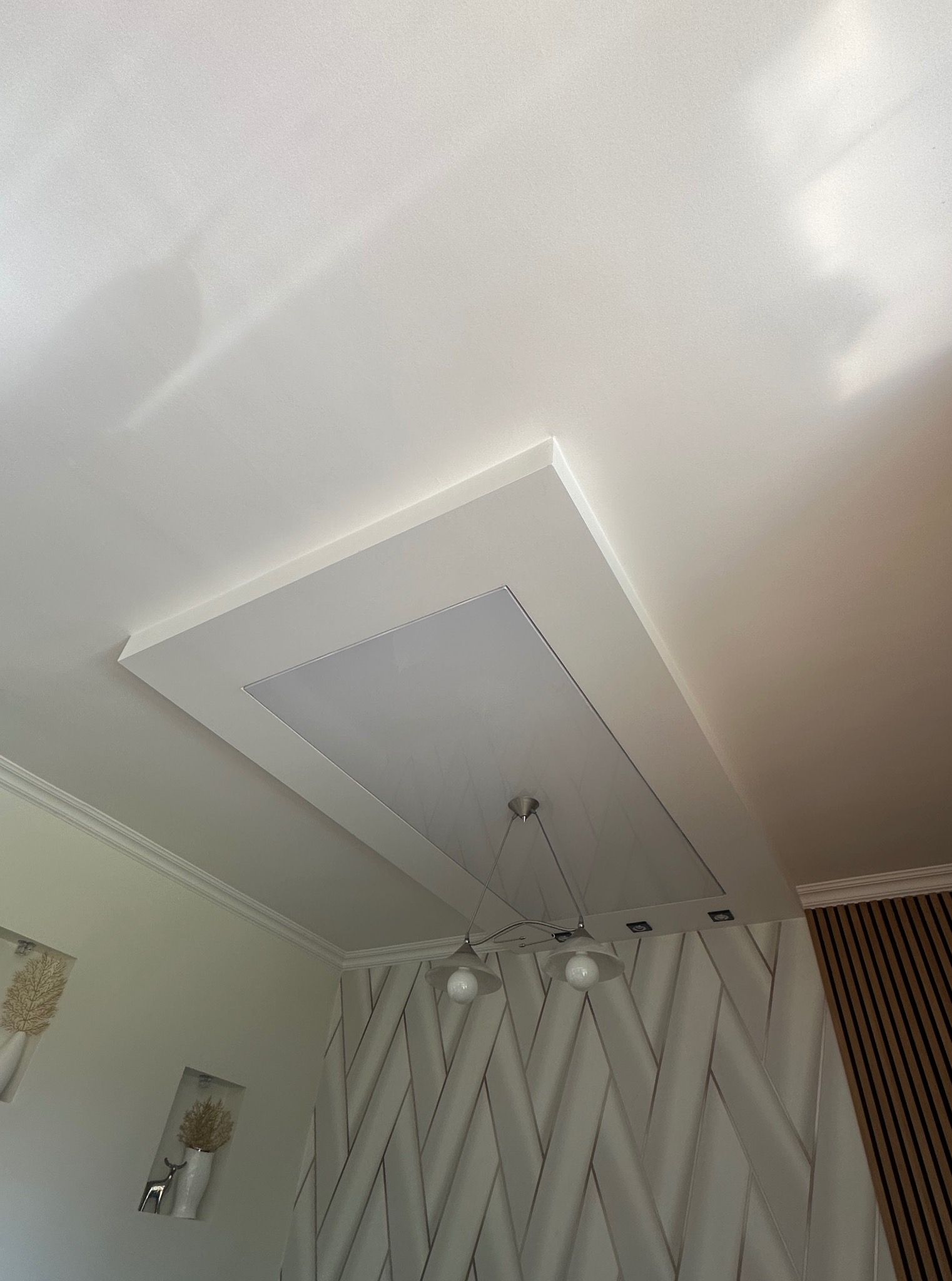 Biały sufit podwieszany z oświetleniem LED, dekoracyjne panele ścienne w tle, nowoczesny design wnętrza, widok z dołu.