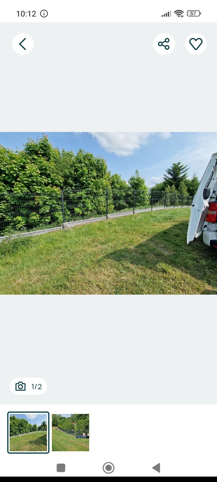 Panelowe ogrodzenie w kolorze grafitowym, z podmurówką, otoczone zielenią i częściowo zasłonięte przez otwarte drzwi samochodu dostawczego.