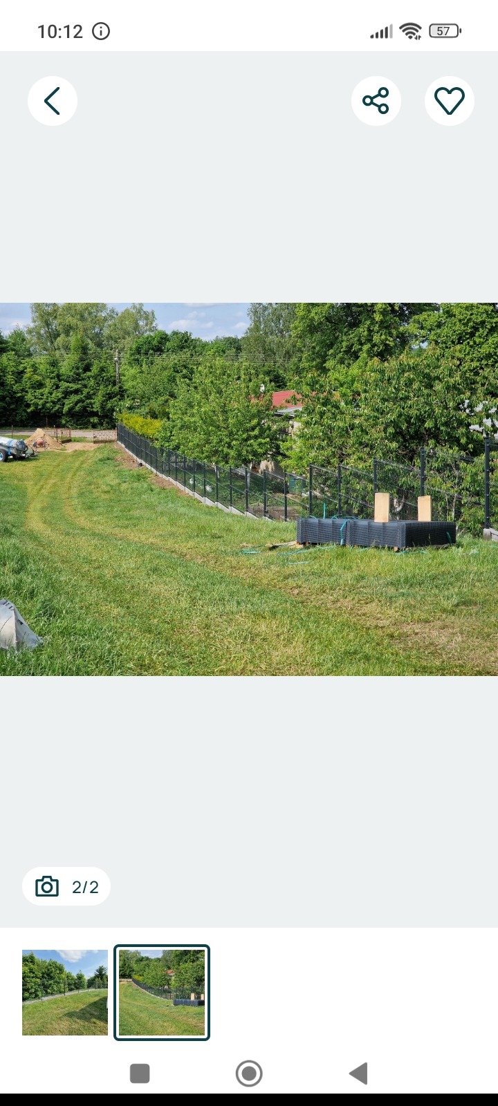 Czarna, panelowa konstrukcja ogrodzeniowa na zielonej działce, z widocznymi elementami montażowymi i drzewami w tle, w słoneczny dzień.