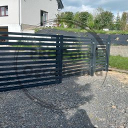 PRO Panel Ogrodzenia - Nowoczesne, poziome przęsła metalowe tworzą ogrodzenie posesji z domem. Fragment otwartej bramy wjazdowej. Szara, żwirowa nawierzchnia.