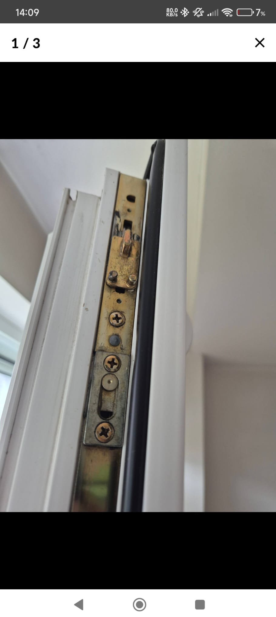 Detal mechanizmu zamka w białym oknie PCV, widoczne śruby krzyżakowe i uszczelka. Ujęcie z bliska, ukazujące zużycie i potencjalną potrzebę naprawy.