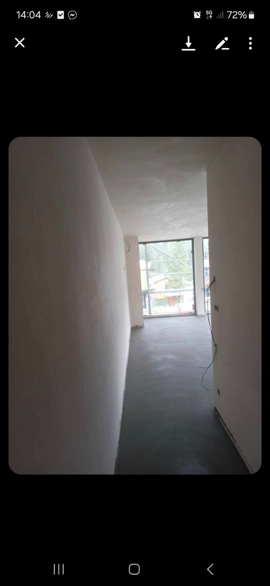 Wnętrze w trakcie prac wykończeniowych. Widoczna świeżo wylana, szara posadzka. Ściany przygotowane do malowania. Okno z widokiem na zieleń.