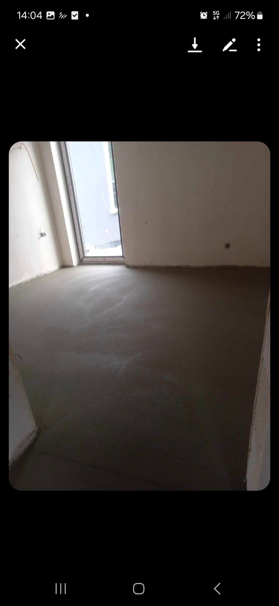 Świeżo wylana, gładka posadzka w jasnym pomieszczeniu z dużym oknem balkonowym. Widoczne ślady po rozprowadzaniu masy.