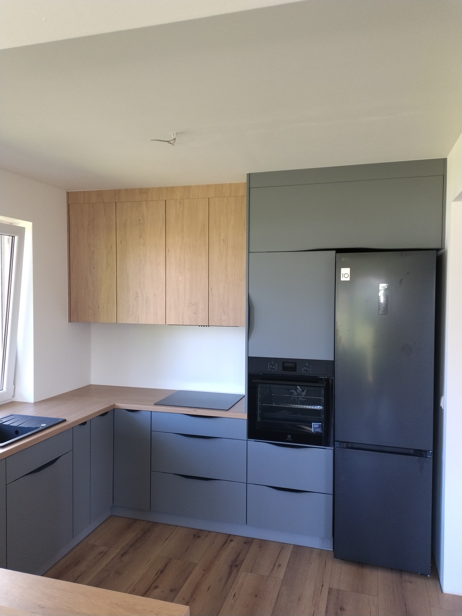 Nowoczesna kuchnia na wymiar w Garbowie: szare szafki dolne z drewnianym blatem, drewniane szafki górne, zabudowana lodówka i piekarnik. Minimalistyczny design.