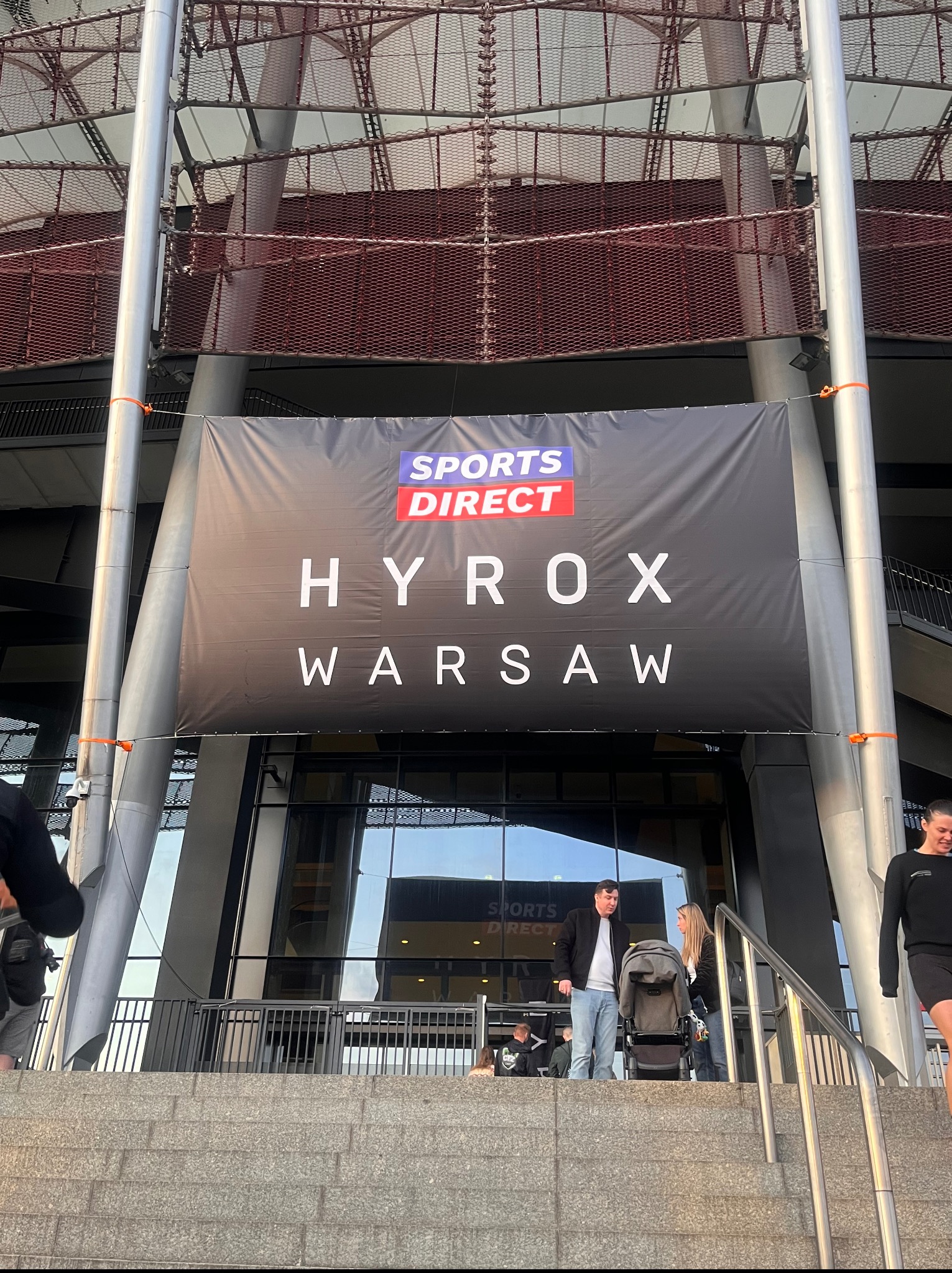 Stadion Narodowy w Warszawie z banerem Sports Direct HYROX Warsaw, widoczne schody, ludzie wchodzący na wydarzenie sportowe.