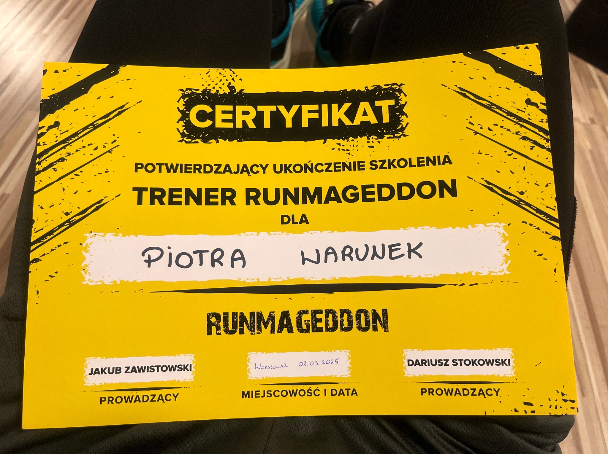 Żółty certyfikat ukończenia szkolenia 'Trener Runmageddon' dla Piotra Warunka, z podpisami prowadzących: Jakuba Zawistowskiego i Dariusza Stokowskiego.