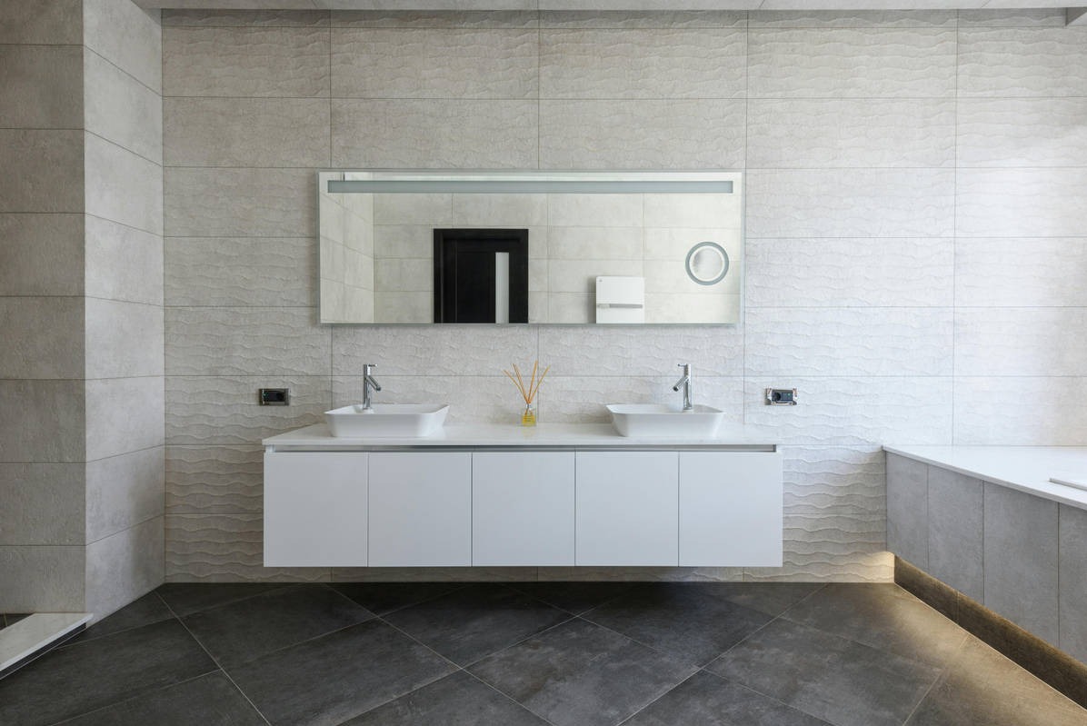 Nowoczesna łazienka z dwoma umywalkami, podświetleniem LED i teksturowanymi płytkami w odcieniach szarości. Minimalistyczny design, lustro z oświetleniem.