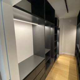 WOBO studio Wojciech Borawski - Nowoczesna, szara szafa wnękowa z oświetleniem LED i szufladami, widok z perspektywy wejścia, na drewnianej podłodze. Minimalistyczny design.