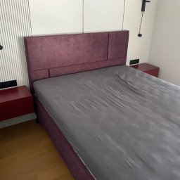 WOBO studio Wojciech Borawski - Fioletowe łóżko z tapicerowanym wezgłowiem, z szarym prześcieradłem, w nowoczesnej sypialni z drewnianą podłogą i szafkami nocnymi w kolorze czerwonego wina.