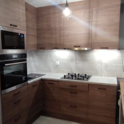 WOBO studio Wojciech Borawski - Nowoczesna kuchnia z drewnianymi frontami, białym blatem i oświetleniem podszafkowym. Widoczny piekarnik, mikrofalówka i płyta gazowa. Wisząca lampa dodaje uroku.