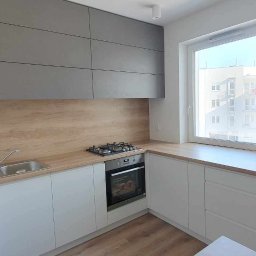 WOBO studio Wojciech Borawski - Jasna kuchnia z szarymi szafkami wiszącymi i drewnianym blatem. Widok na zewnątrz przez okno. Nowoczesny design z minimalistycznym stylem.