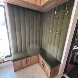 Kącik garderoby z siedziskiem i wieszakami, wykończony zielonym welurem i drewnem, z szafkami nad siedziskiem. Widok z perspektywy podłogi.