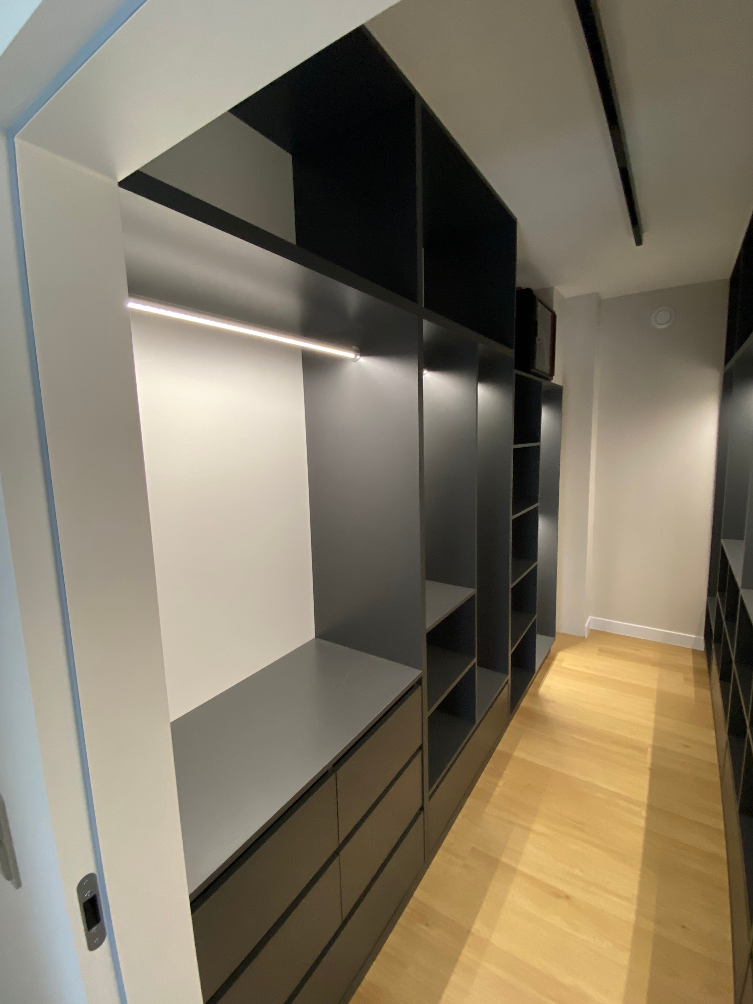 Nowoczesna, szara szafa wnękowa z oświetleniem LED i szufladami, widok z perspektywy wejścia, na drewnianej podłodze. Minimalistyczny design.