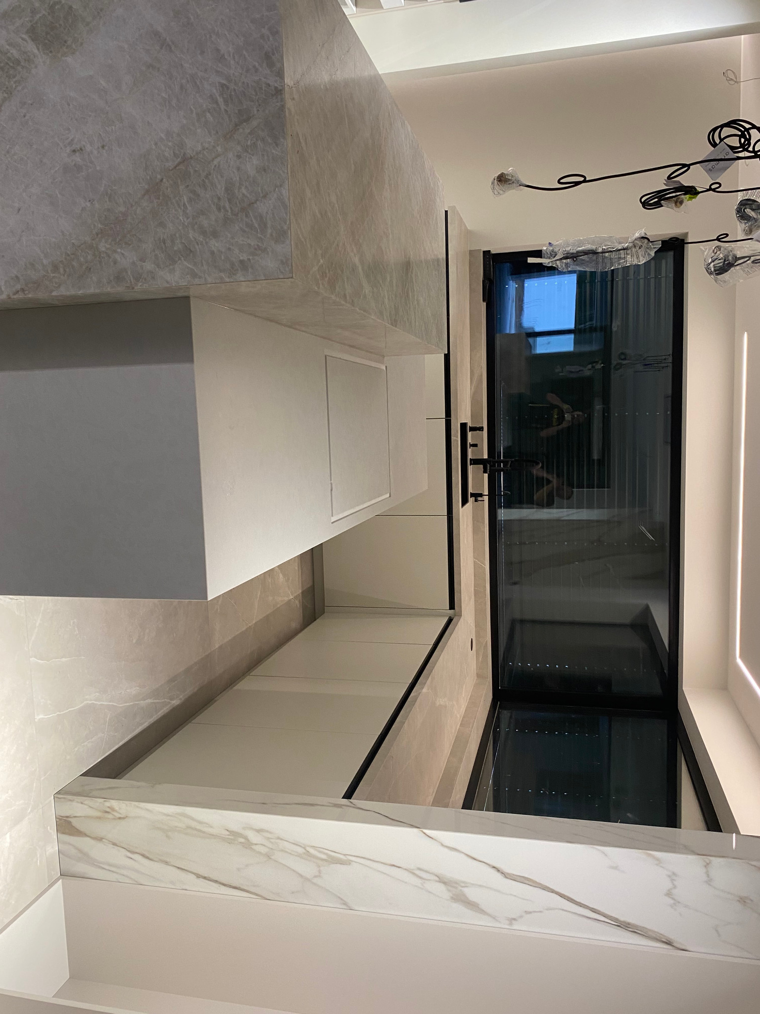 Elegancka szafa wnękowa z marmurowym blatem i czarnymi drzwiami przesuwnymi, oświetlona ledowym światłem, tworząca nowoczesny design wnętrza.