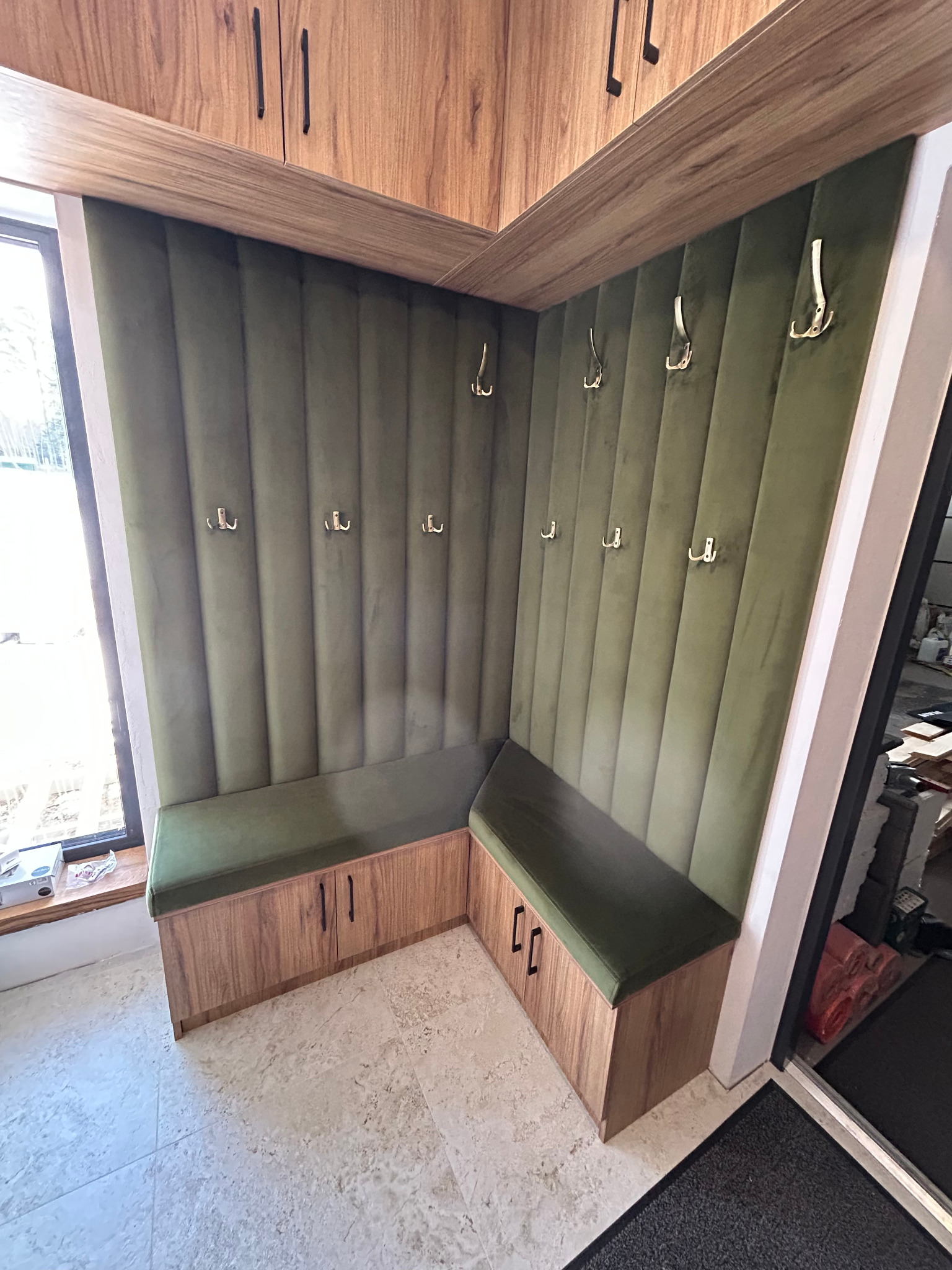 Kącik garderoby z siedziskiem i wieszakami, wykończony zielonym welurem i drewnem, z szafkami nad siedziskiem. Widok z perspektywy podłogi.