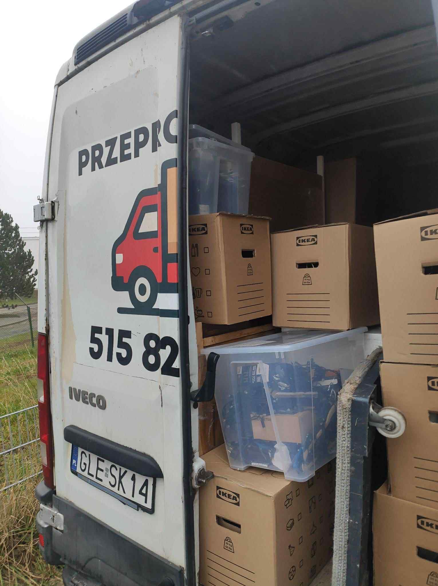 Załadunek kartonów IKEA i plastikowych pojemników do białego busa z logo firmy przeprowadzkowej. Widoczny numer telefonu i tablica rejestracyjna.