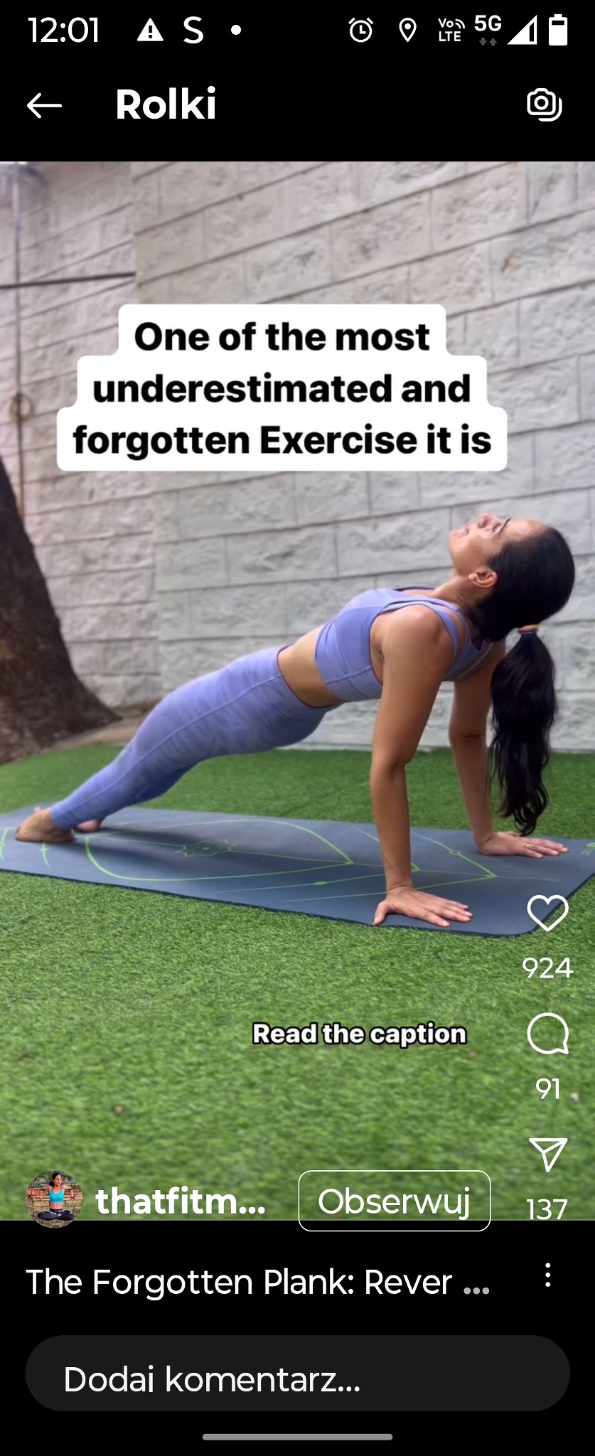 Kobieta w sportowym stroju wykonuje odwróconą deskę na macie do ćwiczeń na tle ściany z cegły i trawy. Widoczne elementy interfejsu aplikacji.