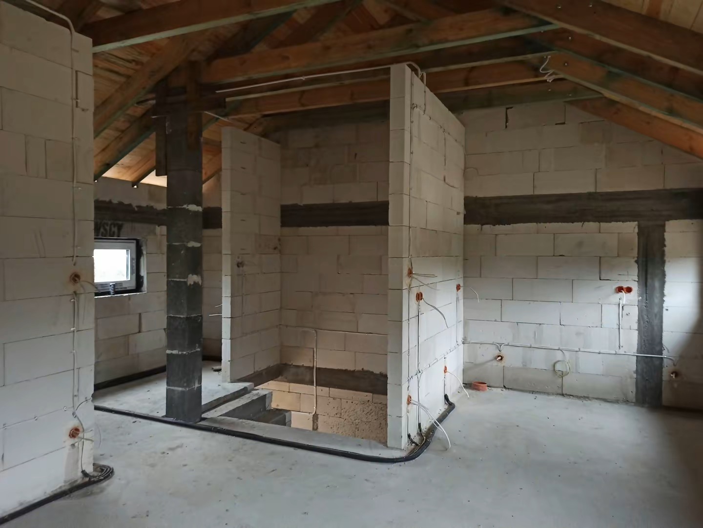 Surowy stan poddasza w Kosakowie: ściany z betonu komórkowego, widoczne przewody elektryczne, przygotowane do dalszych prac wykończeniowych.