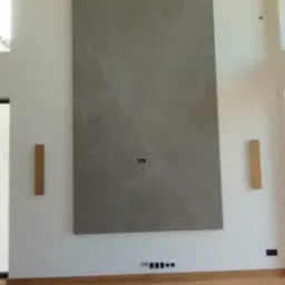 Wysoka ściana z szarych, marmurkowych płytek w salonie, z drewnianą podłogą i elementami dekoracyjnymi. Minimalistyczny design, nowoczesne wykończenie.