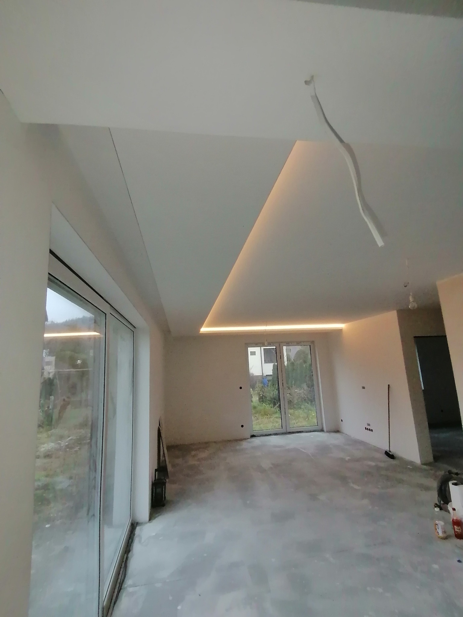 Nowoczesne wnętrze w trakcie wykończenia: gładkie ściany i sufit z oświetleniem LED, duże okna z widokiem na zewnątrz. Podłoga w trakcie prac.