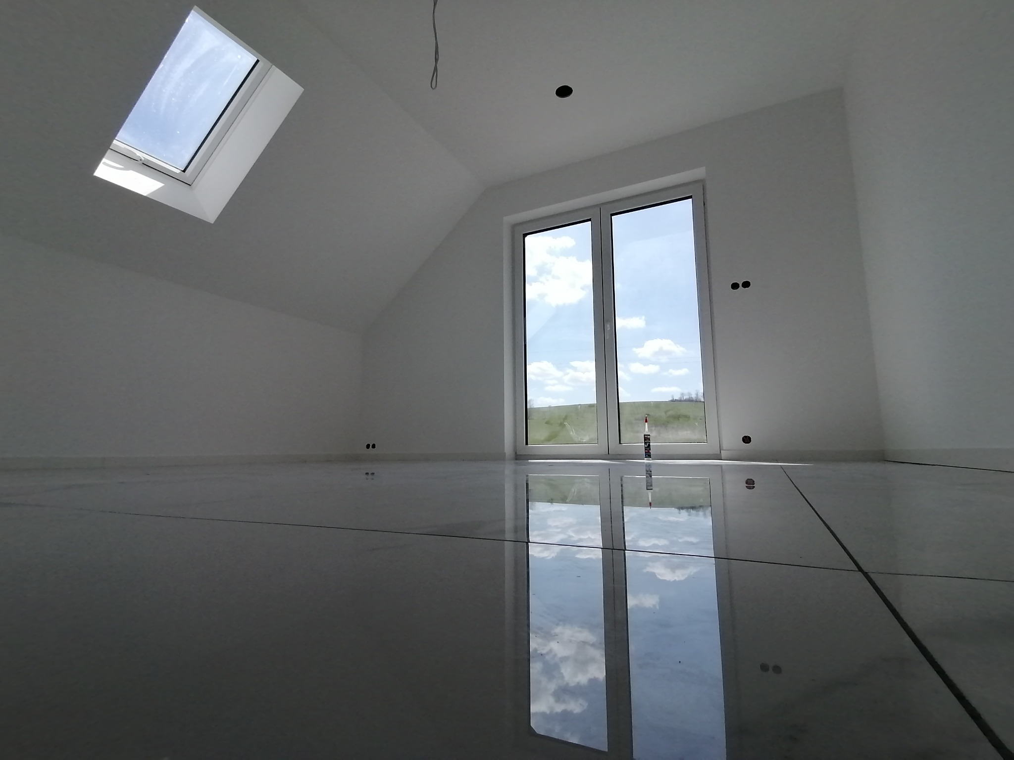 Jasne poddasze po remoncie: białe ściany, błyszcząca podłoga z płytek odbijająca niebo. Widoczne okno dachowe i balkonowe. Minimalistyczny design.