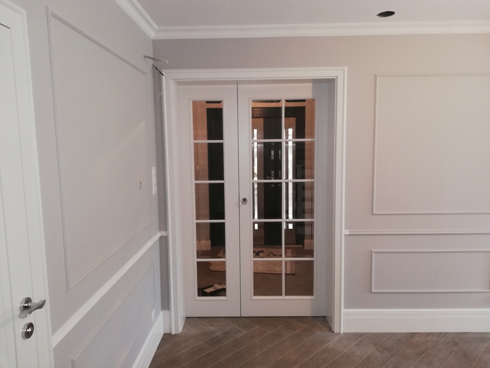 Jasne wnętrze z podwójnymi, przeszklonymi drzwiami. Ściany zdobione sztukaterią, parkiet ułożony w jodełkę. Widoczne detale wykończeniowe, listwy przypodłogowe.