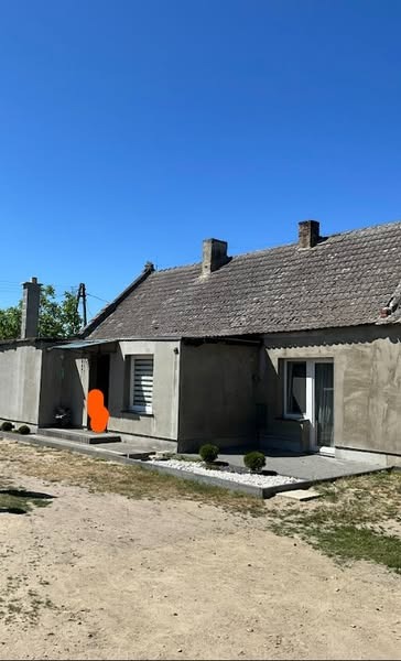 Niski dom jednorodzinny z szarą elewacją, widoczny z perspektywy ogrodu, z elementami dekoracyjnymi z białego kamienia i zielonymi krzewami.