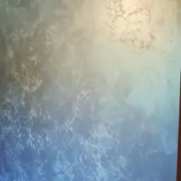 Dekoracyjna ściana z efektem marmuru w odcieniach błękitu i szarości, oświetlona z góry, z widoczną fakturą i nieregularnymi wzorami. Wykończenie wnętrz.