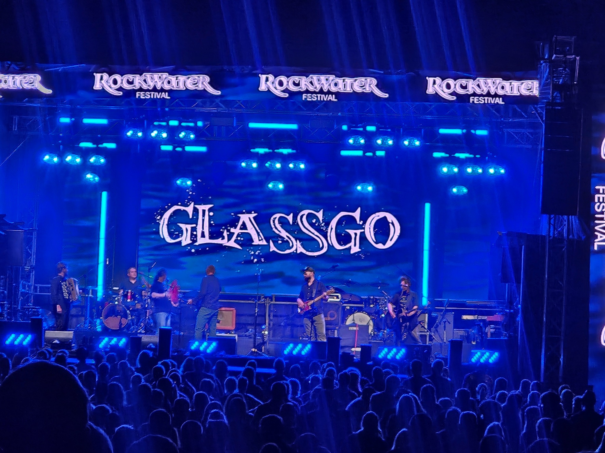 Zespół GlassGo na scenie Rockwater Festival oświetlonej niebieskimi światłami. Widoczny tłum fanów.