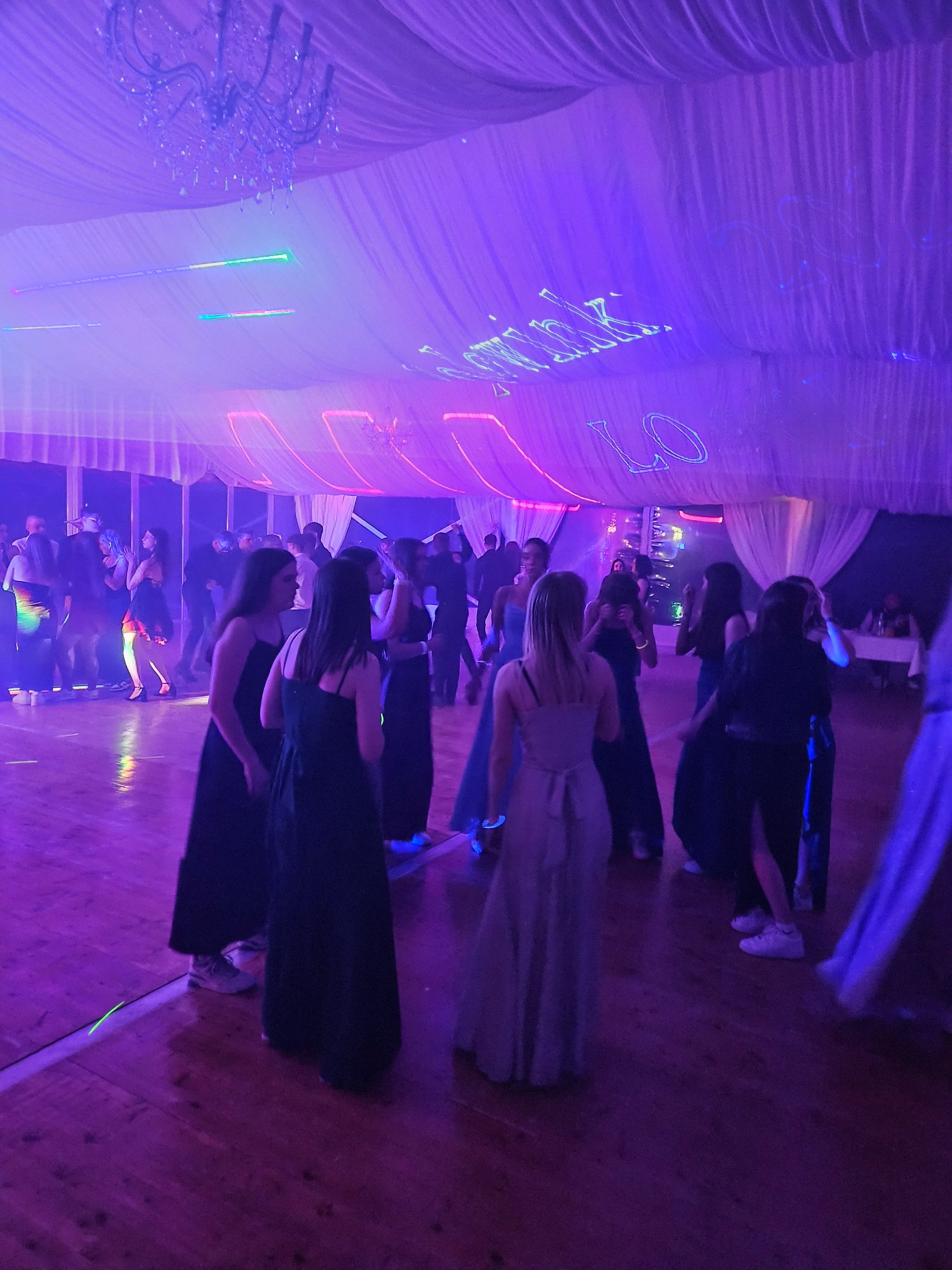 Zabawa taneczna w fioletowym oświetleniu. Parkiet wypełniony tańczącymi osobami, dekoracyjne oświetlenie i materiałowe dekoracje sufitu tworzą imprezowy klimat.