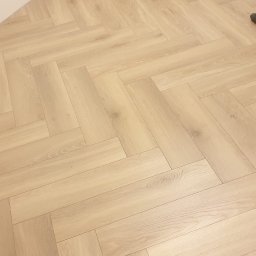 Good joob - Jasne panele ułożone w jodełkę, widoczne narzędzia pracy w rogu pomieszczenia, ściana w trakcie wykończenia.