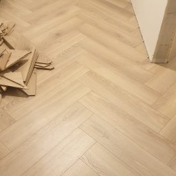 Good joob - Jasne panele ułożone we wzór jodełki francuskiej, z widocznymi resztkami materiału i workiem, sugerujące etap prac wykończeniowych w pomieszczeniu.