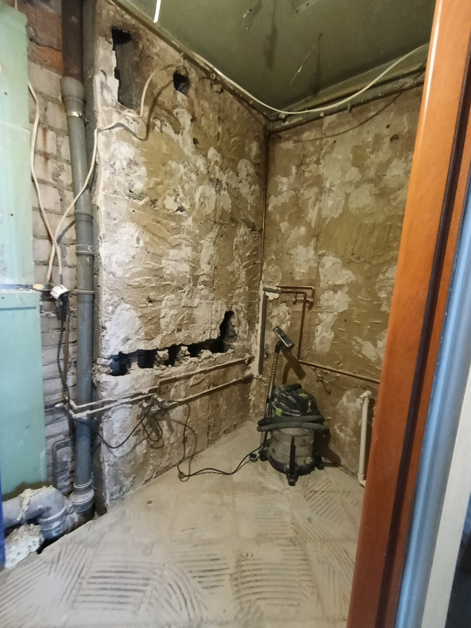 Łazienka w trakcie remontu: odsłonięte mury, widoczne rury, instalacje i odkurzacz przemysłowy. Przygotowanie do dalszych prac wykończeniowych.