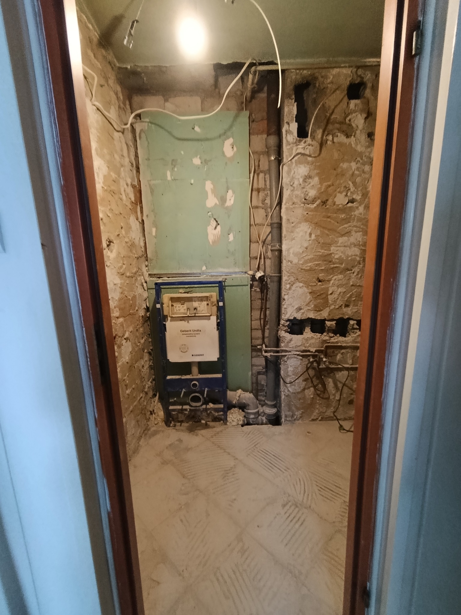 Łazienka w trakcie remontu: widoczne odsłonięte ściany, instalacja podtynkowa Geberit, przygotowana podłoga pod płytki, surowy stan przed wykończeniem.