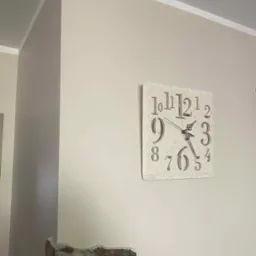 Jasna ściana po malowaniu z dekoracyjnym zegarem. Widoczny fragment kamiennej dekoracji ściany. Neutralna kolorystyka wnętrza, wykończenie listwą przysufitową.