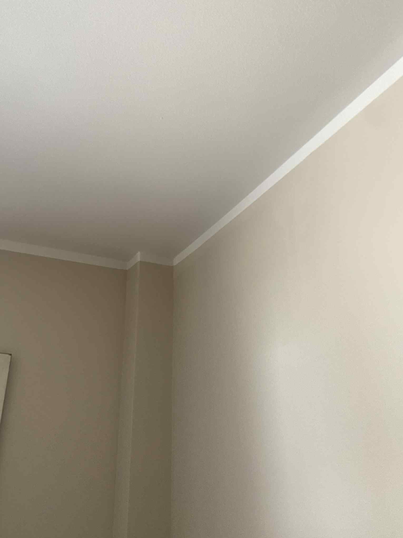 Pomieszczenie po malowaniu z dekoracyjną, białą listwą przysufitową, widok na róg pokoju. Ściany w odcieniach beżu i bieli, gładkie powierzchnie.