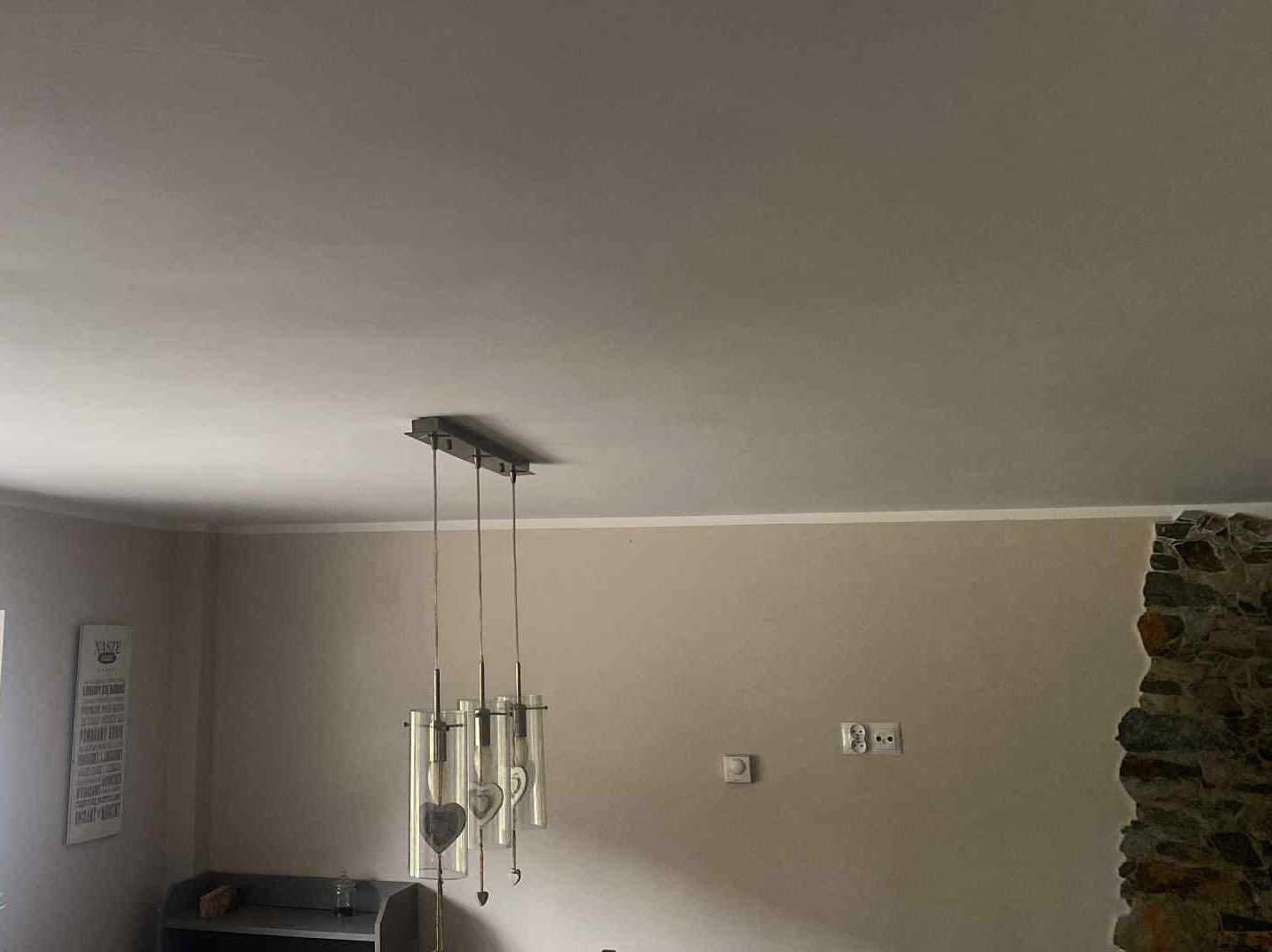 Gładko wyszpachlowany sufit w beżowym wnętrzu z dekoracyjnym oświetleniem. Widoczne gniazdka elektryczne i fragment ściany z kamienną okładziną.