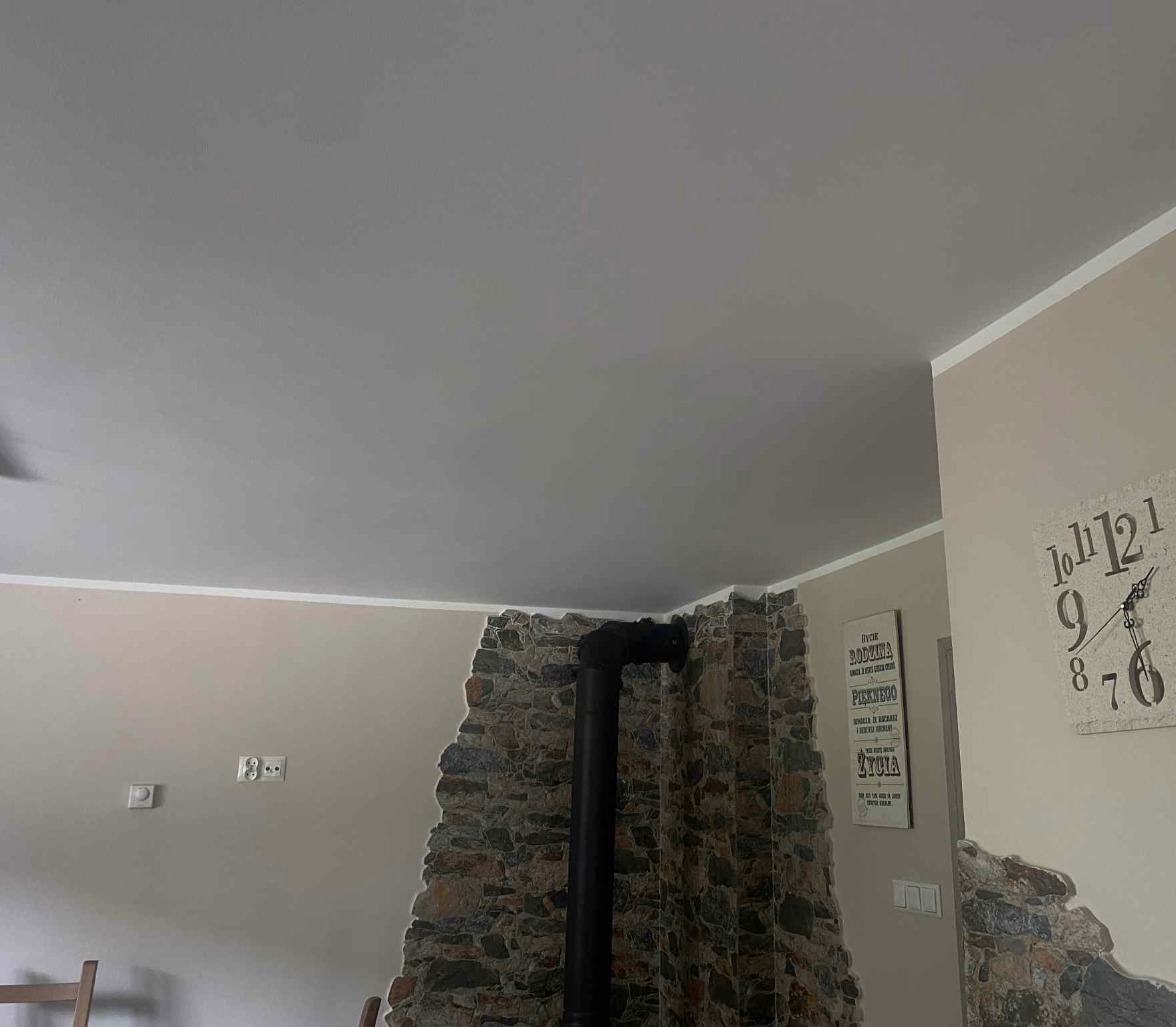 Jasne wnętrze z dekoracyjnym obłożeniem ściany kamieniem wokół komina i zegarem. Widoczne gładkie ściany i sufit.