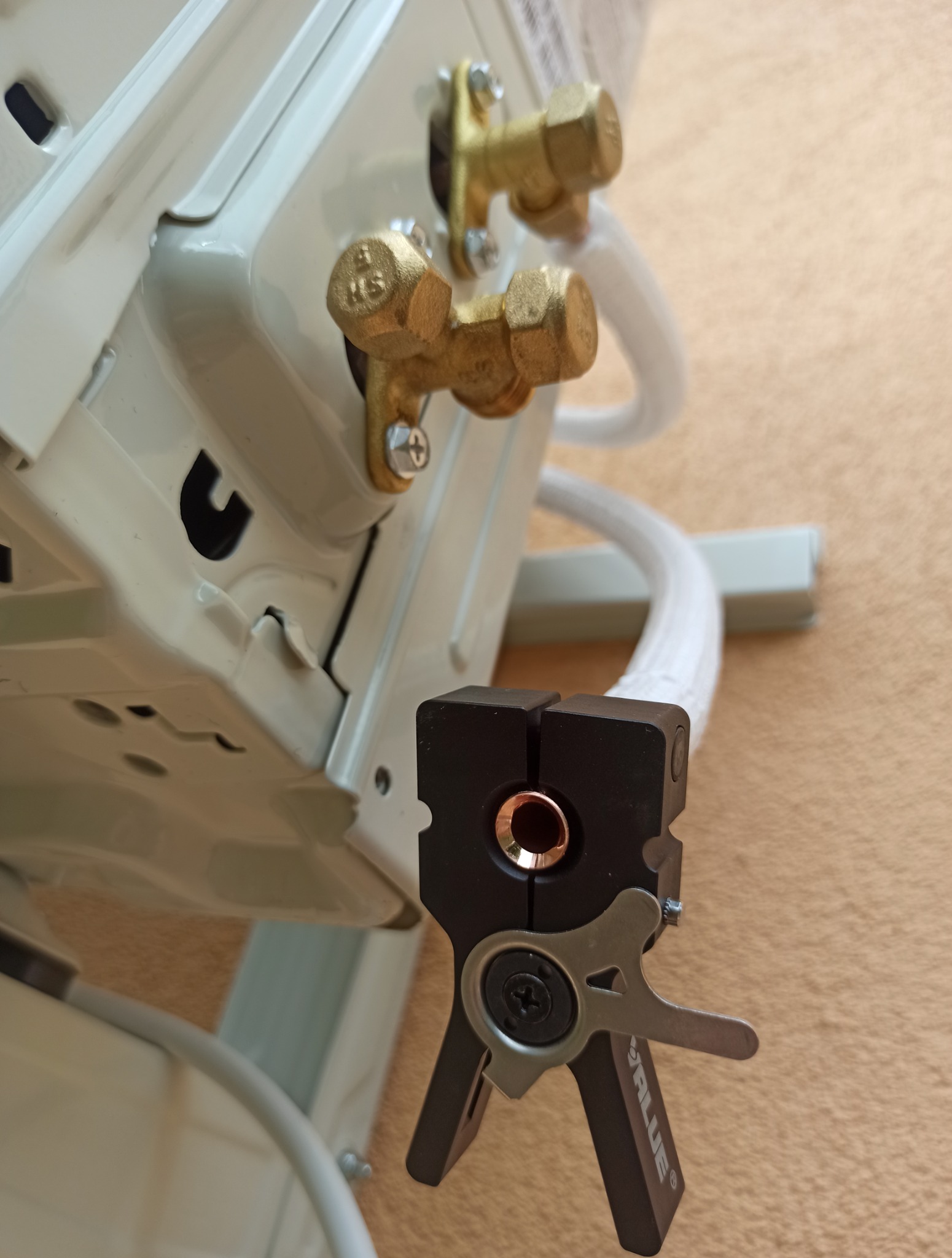 Klimatyzator w trakcie montażu: widoczne miedziane złączki, biała rurka i czarny zaciskarka do rur. Detal instalacji klimatyzacji.