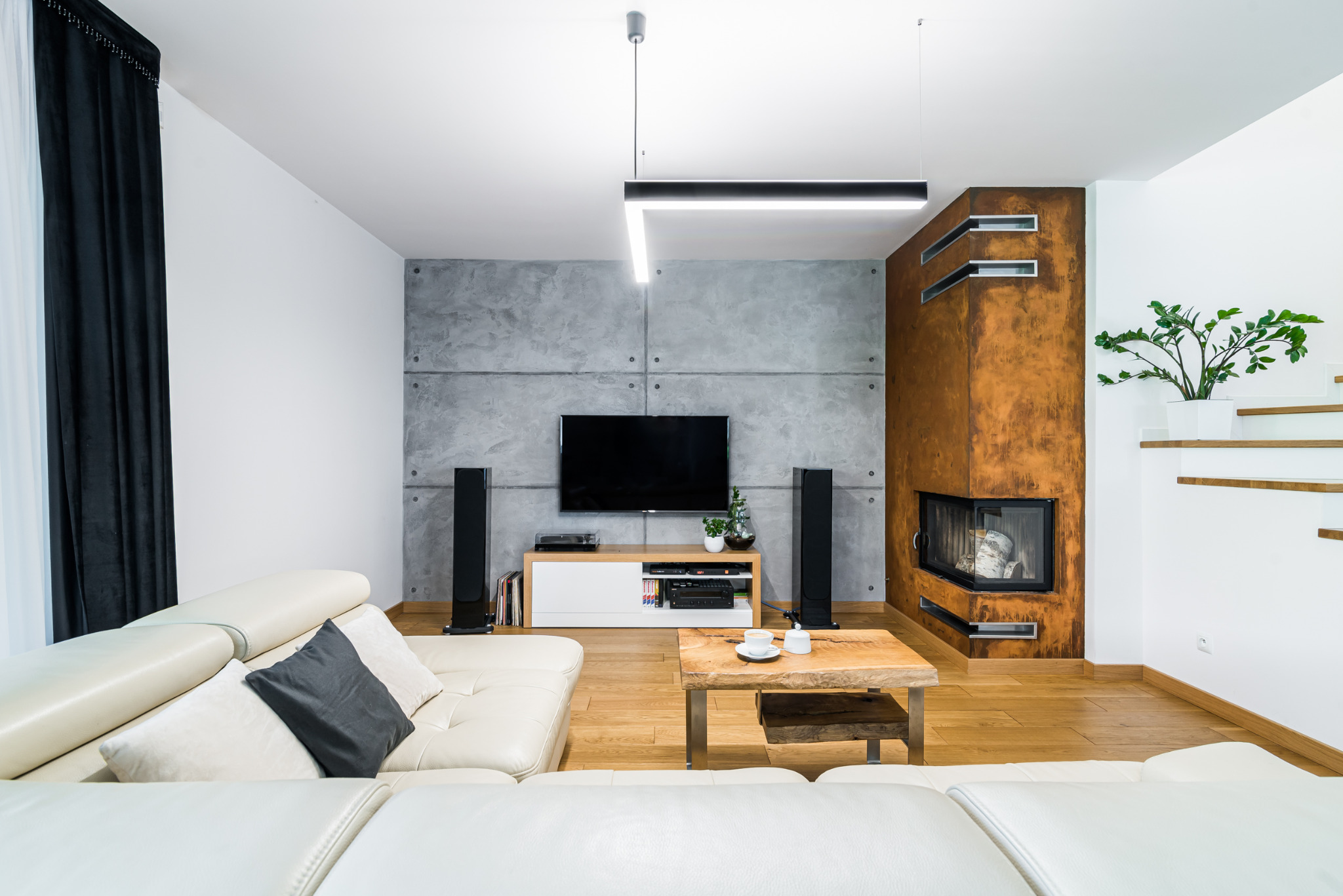 Jasny salon z betonową ścianą, telewizorem, kominkiem i drewnianym stolikiem kawowym. Nowoczesne wnętrze z sofą ze skóry w odcieniach bieli.