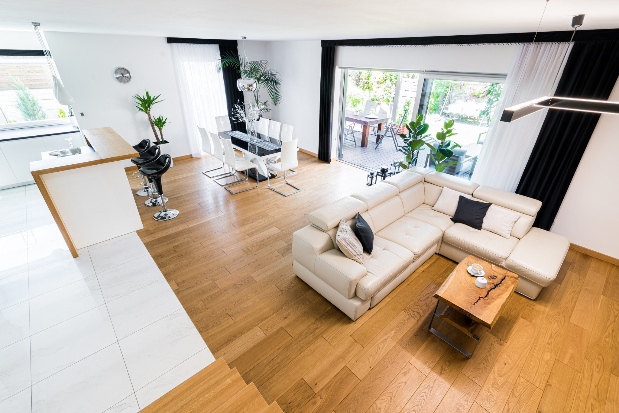 Jasne, przestronne wnętrze z drewnianą podłogą, białym narożnikiem i otwartą przestrzenią na zewnątrz. Widok z góry podkreśla nowoczesny design i naturalne światło.