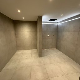 Adrian Brzozowski - Wykończona, nowoczesna łazienka z beżowymi płytkami, oświetleniem LED na suficie i punktowymi lampami. Widoczny otwór w suficie, prawdopodobnie na wentylator.