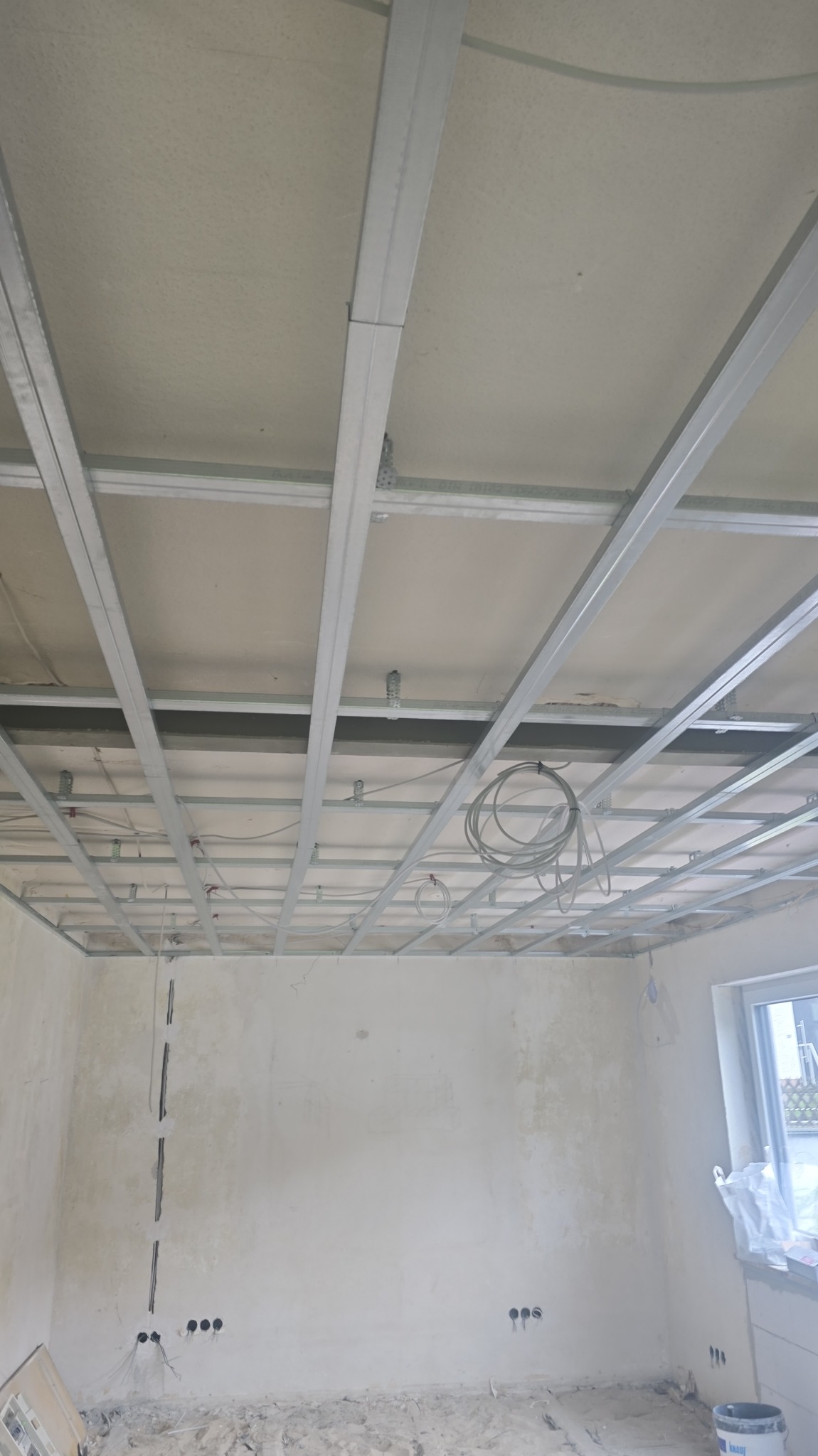 Sufit podwieszany z metalową konstrukcją i instalacją elektryczną w surowym wnętrzu pokoju podczas remontu. Widoczne kable i puszki elektryczne.