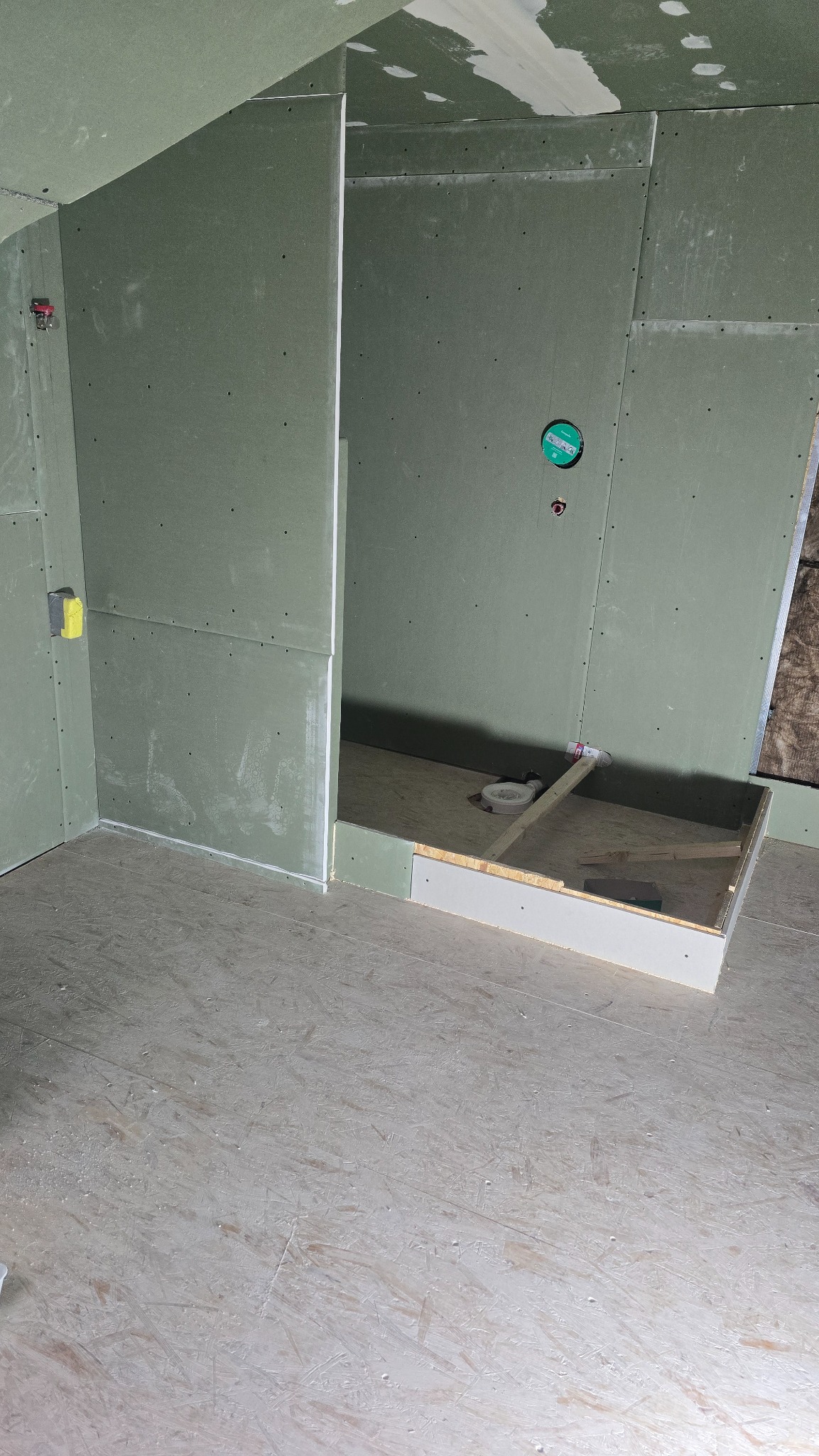 Montaż płyt gipsowo-kartonowych w łazience, widoczna konstrukcja brodzika i instalacja odpływowa. Ściany przygotowane do dalszych prac wykończeniowych.