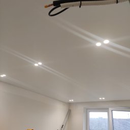 INSPIRATION BEAUTY Sp. z o.o. - Biały sufit z zamontowanymi punktowymi lampami LED. Widoczna instalacja elektryczna w peszlu i fragment drabiny. W tle okno z widokiem na budynek.