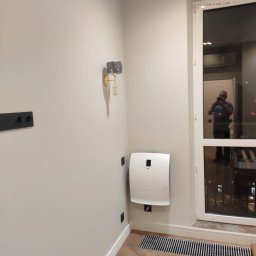 INSPIRATION BEAUTY Sp. z o.o. - Minimalistyczne wnętrze: beżowe ściany, parkiet w jodełkę, nowoczesny grzejnik, designerski kinkiet i okno z odbiciem fotografa.