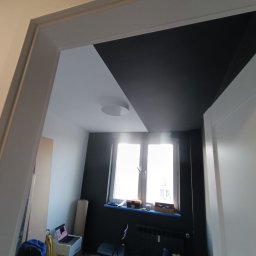 INSPIRATION BEAUTY Sp. z o.o. - Pomieszczenie po malowaniu: czarna ściana kontrastuje z białą, sufit podzielony na biało-czarne strefy. Okno z widokiem na zewnątrz. Widoczny grzejnik i elementy wyposażenia.