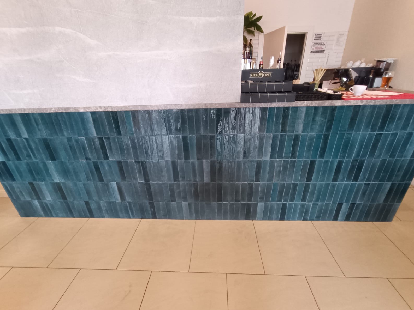 Turkusowa ściana z wąskich płytek ułożonych pionowo, z szarą płytą na górze. Na ścianie widoczne refleksy światła, a na górze elementy wyposażenia wnętrza.