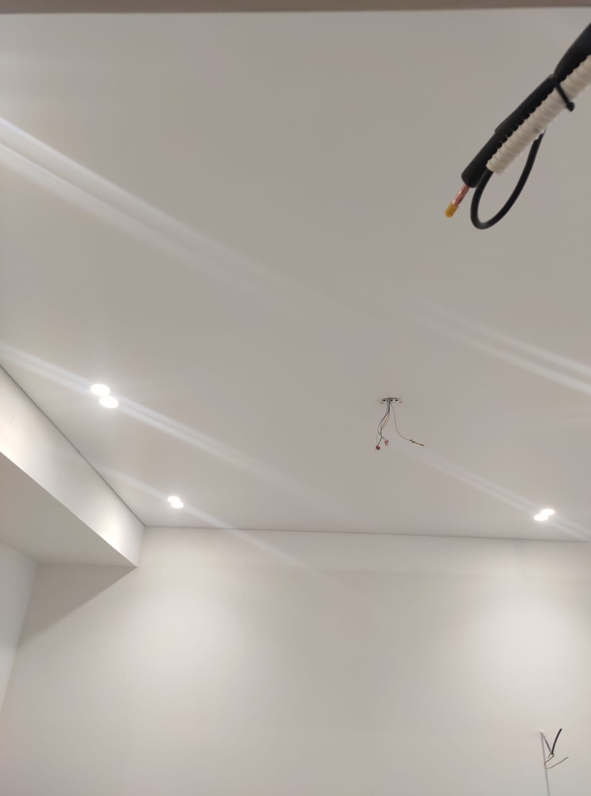 Białe wnętrze z zamontowanym oświetleniem punktowym w suficie podwieszanym. Widoczne wystające przewody i fragment instalacji klimatyzacji.