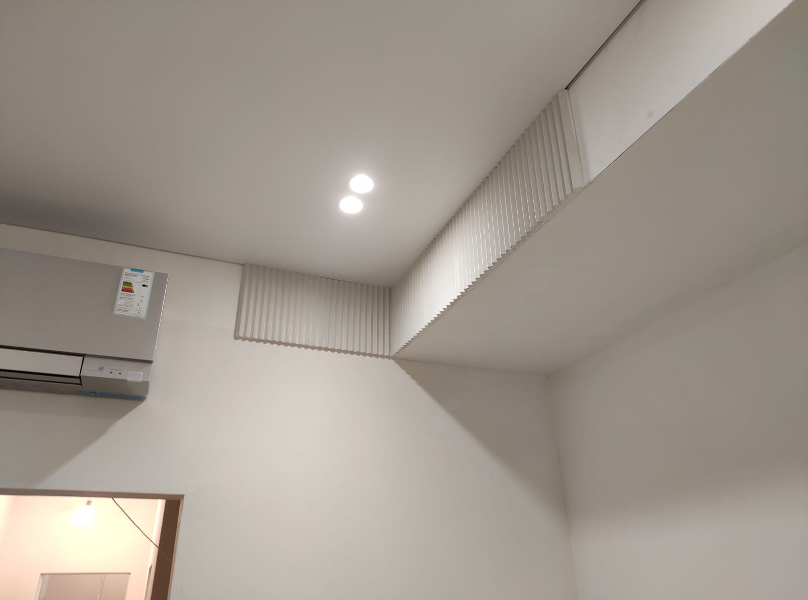 Białe, nowoczesne wnętrze z klimatyzacją i dekoracyjnymi lamelami na suficie, oświetlone dwoma punktowymi lampami. Minimalistyczny design.